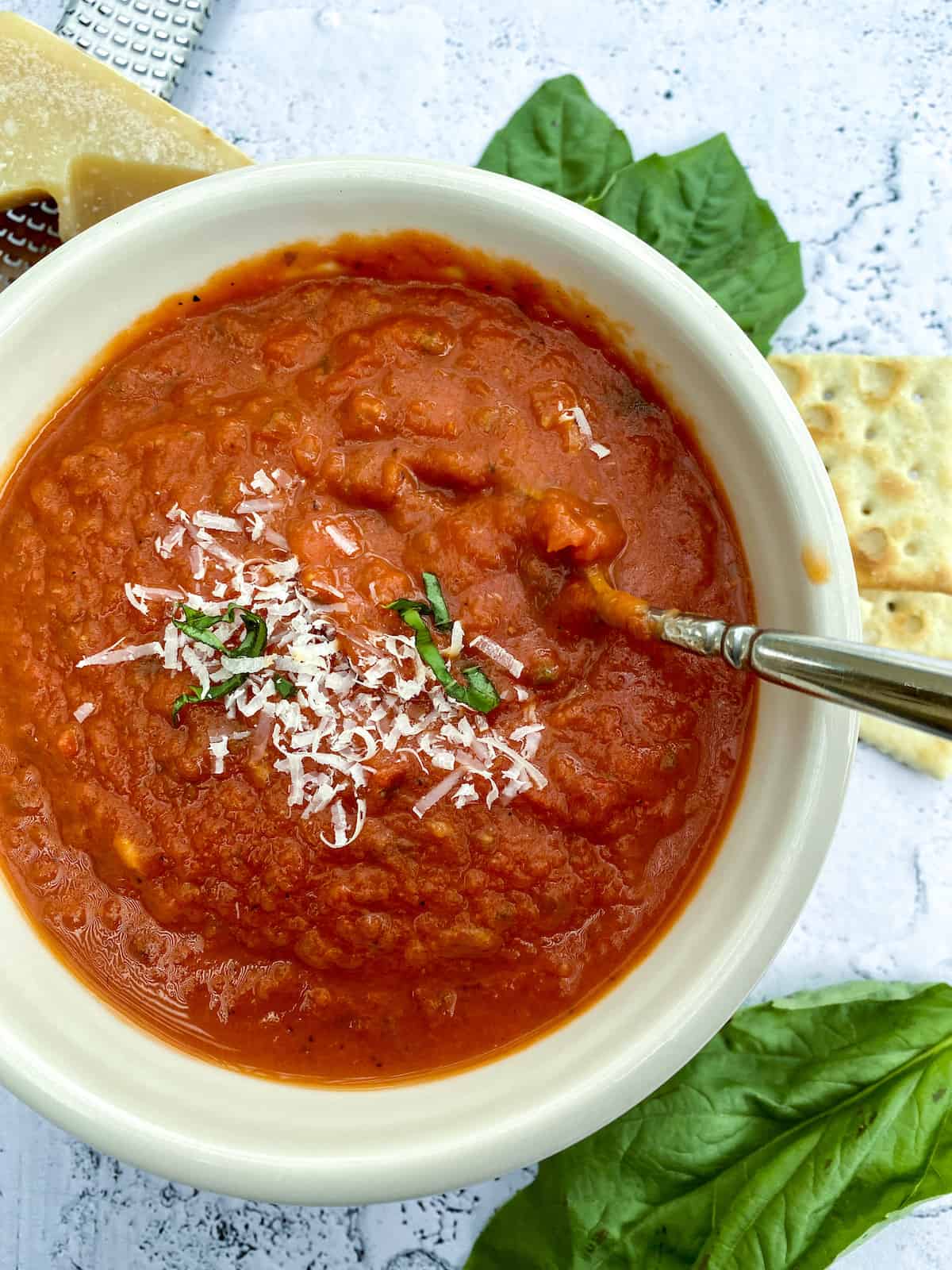 A bowl of tomato basil soup with crackers, cheese and basil on the side.