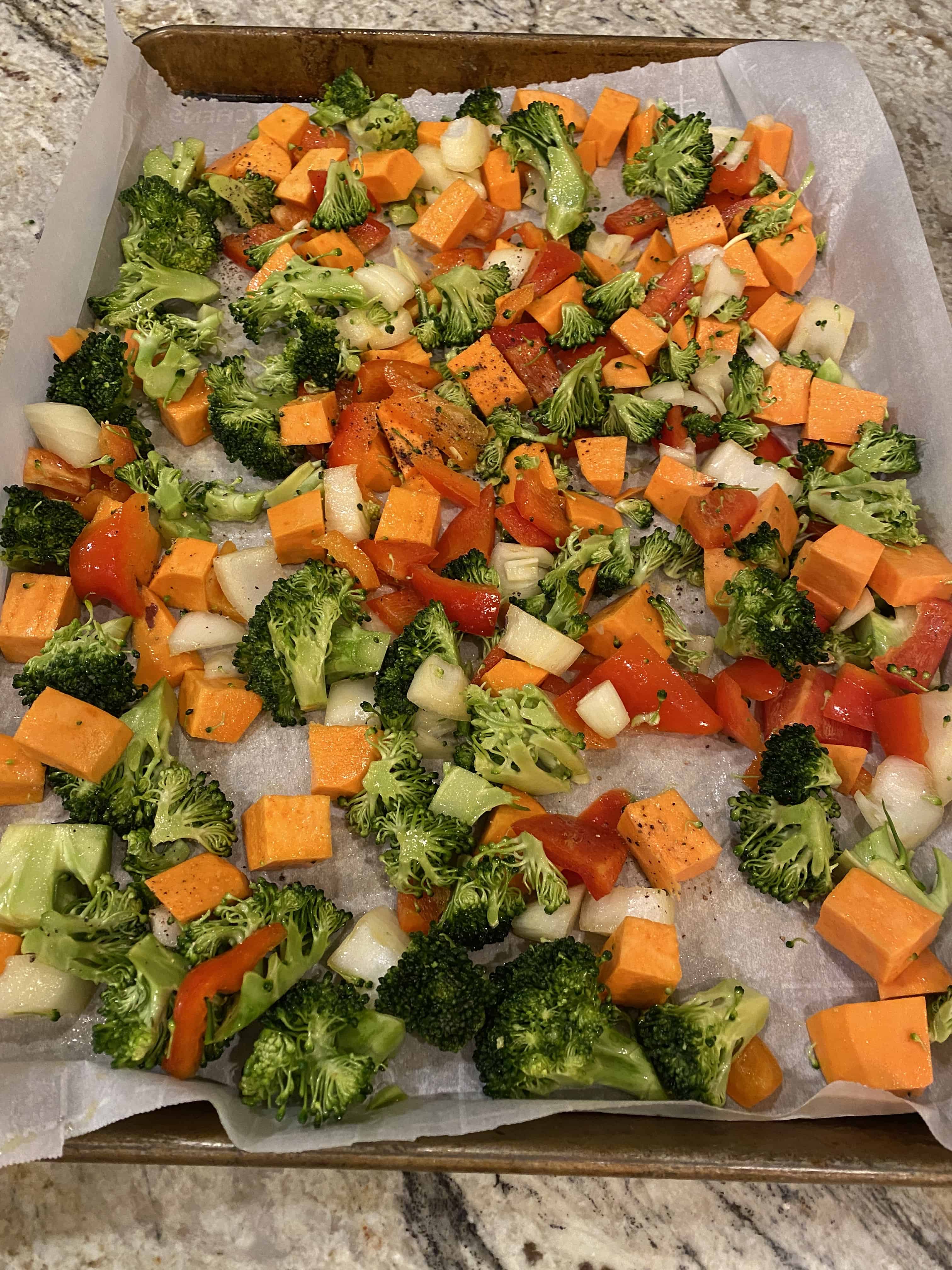 A mix of veggies spread out on a piece of parchment paper on a baking sheet.