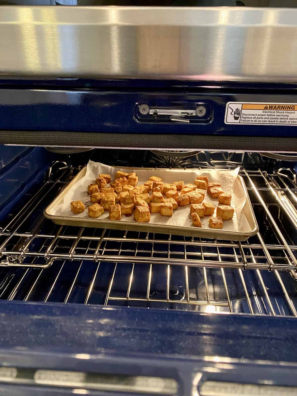 A baking sheet in the oven, with diced tofu arranged on parchment paper.