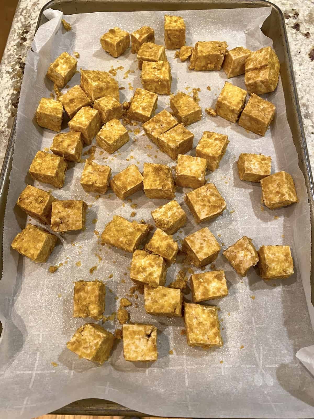 Diced tofu arranged on parchment paper on a baking sheet.