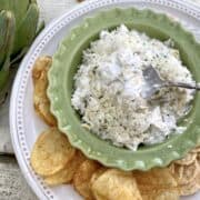 A large plate with chips and crackers and a small bowl of artichoke dip in the center.