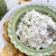 A small bowl with dip, chips on the side and a spoon scooping up a serving of dip.