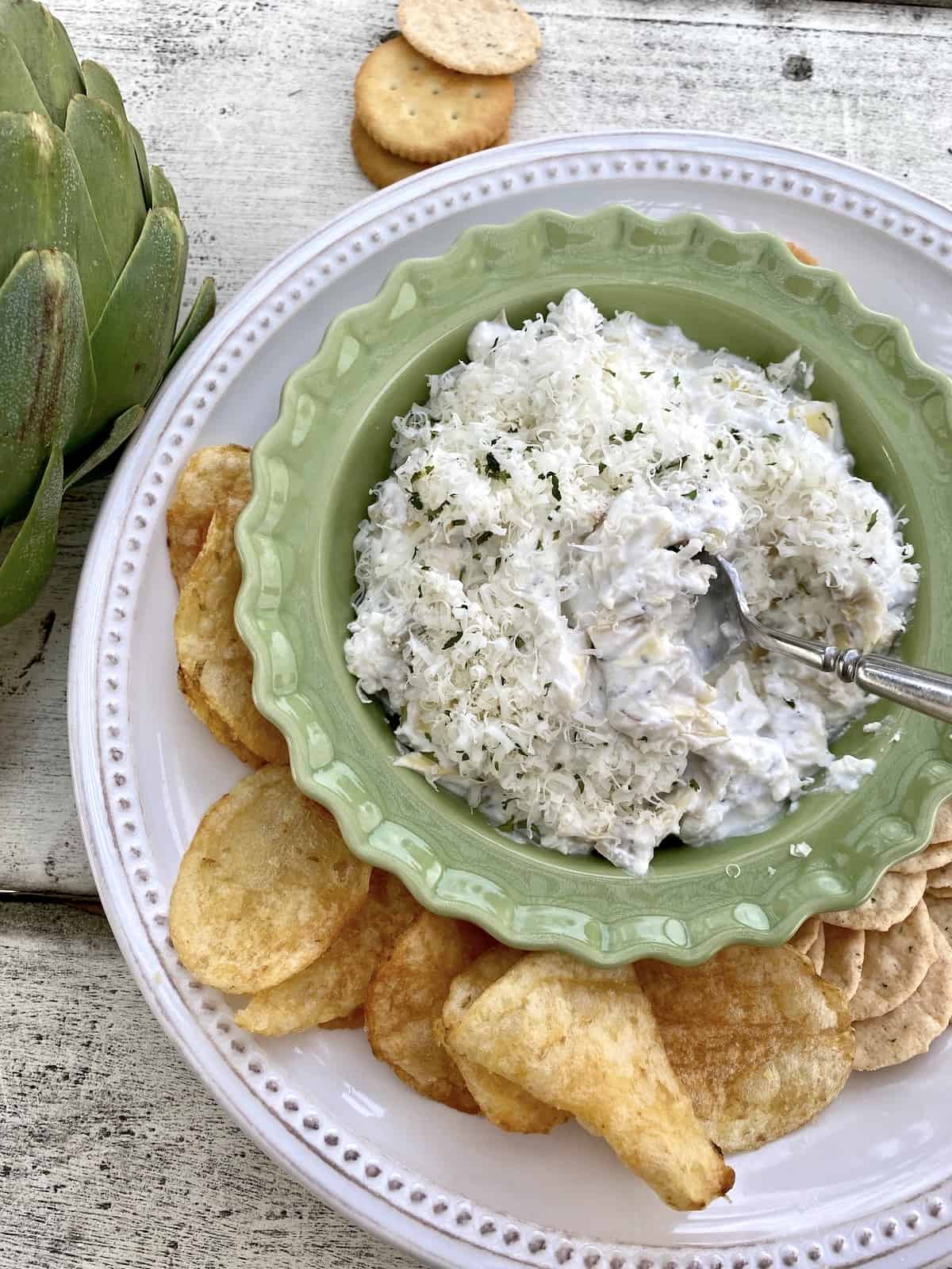 Hot artichoke dip on a platter with chips and crackers.