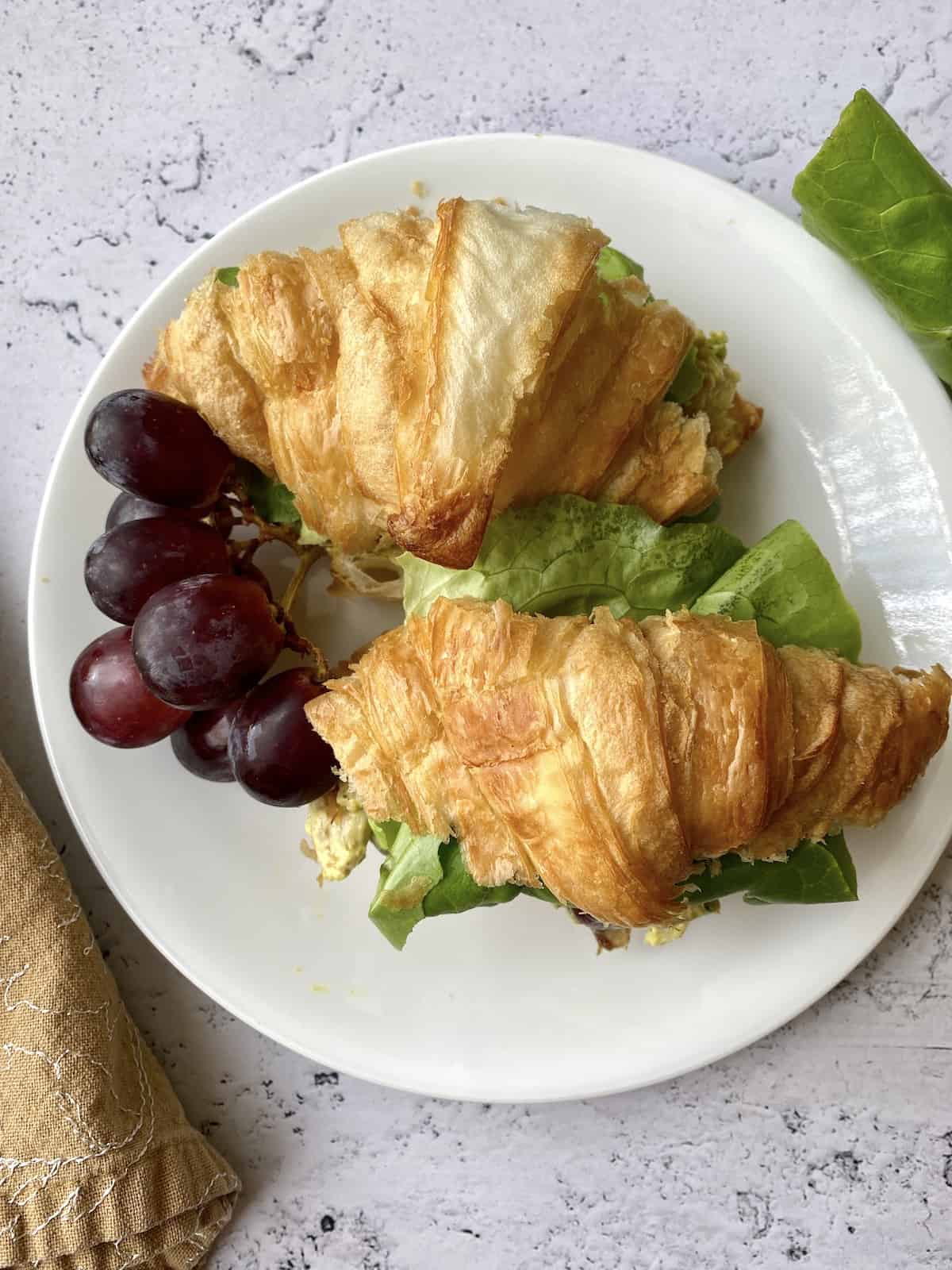 Two croissants filled with chicken curry and grapes on the side. 