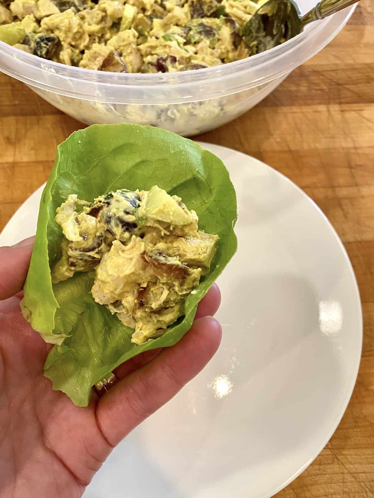 Chicken curry on a lettuce wrap, being held over a plate. 
