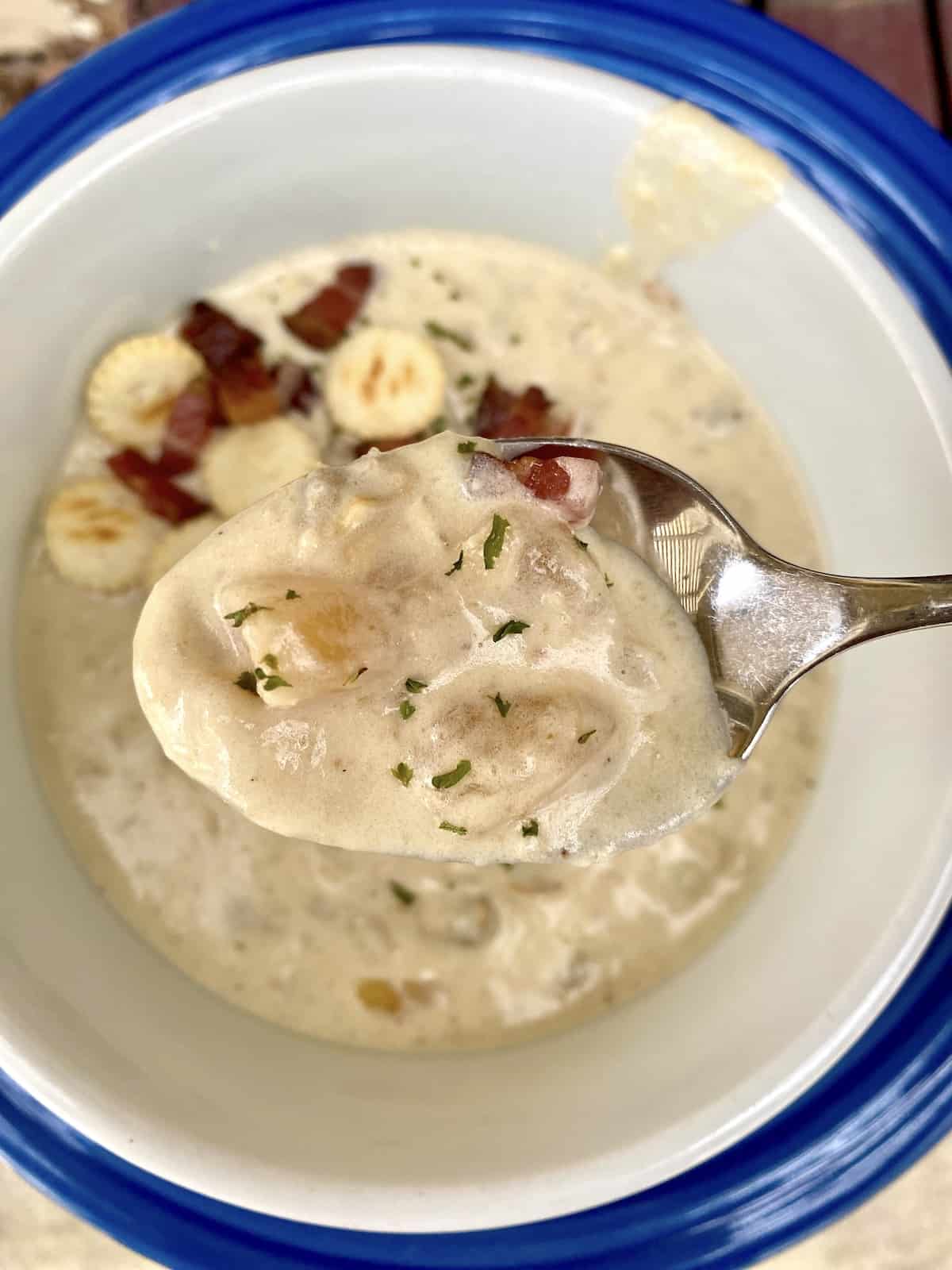 A spoonful of clam chowder, with crackers and bacon bits on the surface of the chowder in the bowl.