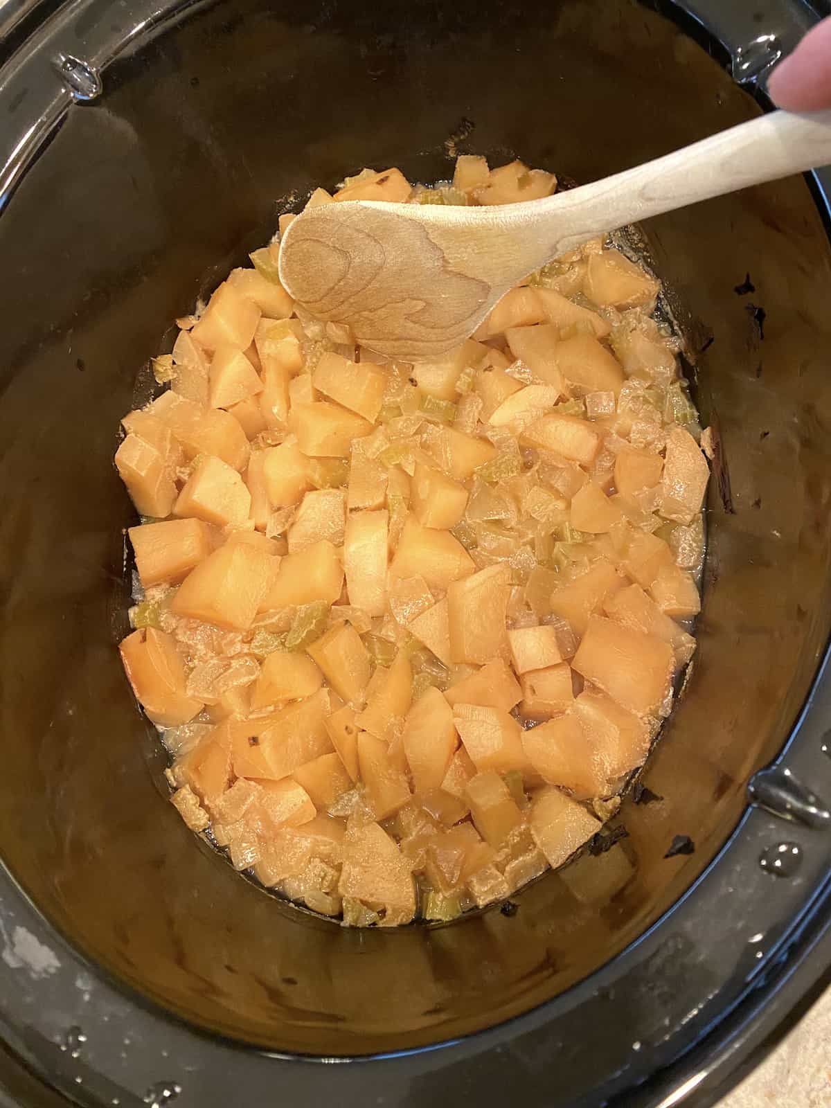 Cooked potatoes and celery in a crockpot with a wooden spoon on the side of the pot.