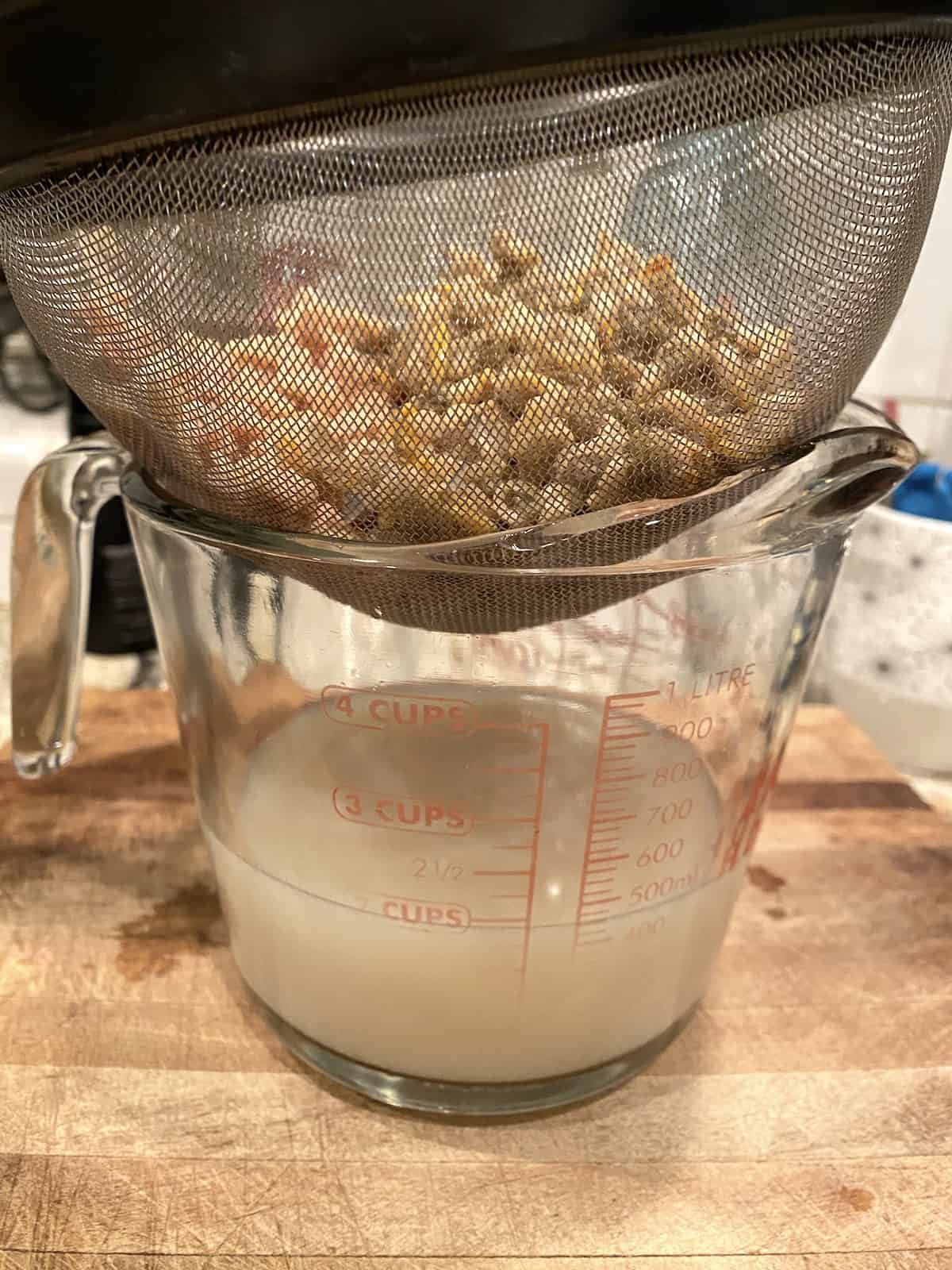 Clams in a small strainer over a measuring cup with juice collecting in the cup.