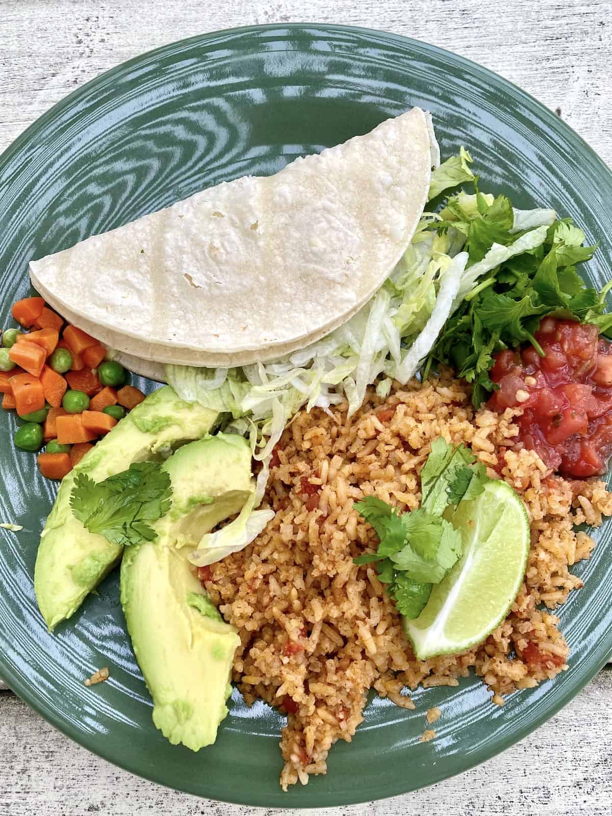 A plate with a serving of Mexican rice, topped with lime and avocado, peas and carrots and salsa on the side.