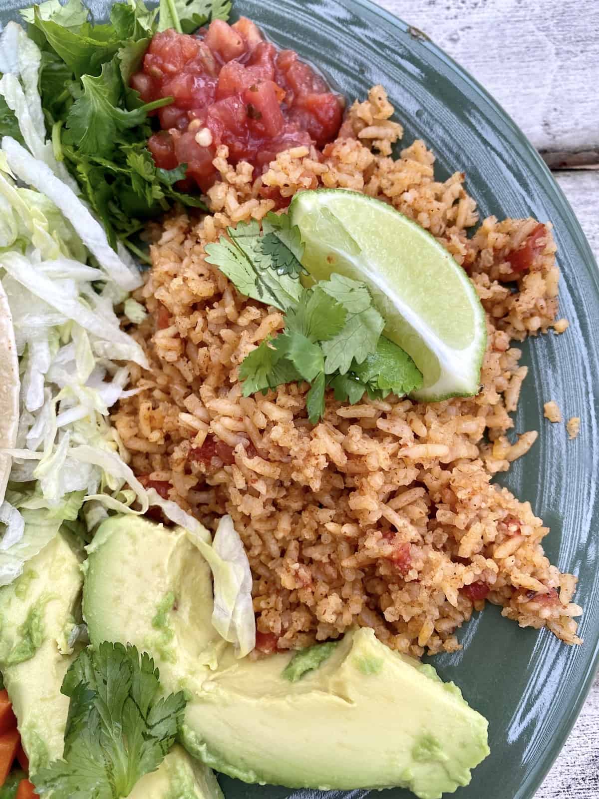 Mexican rice on a plate with avocado on the side, topped with lime.