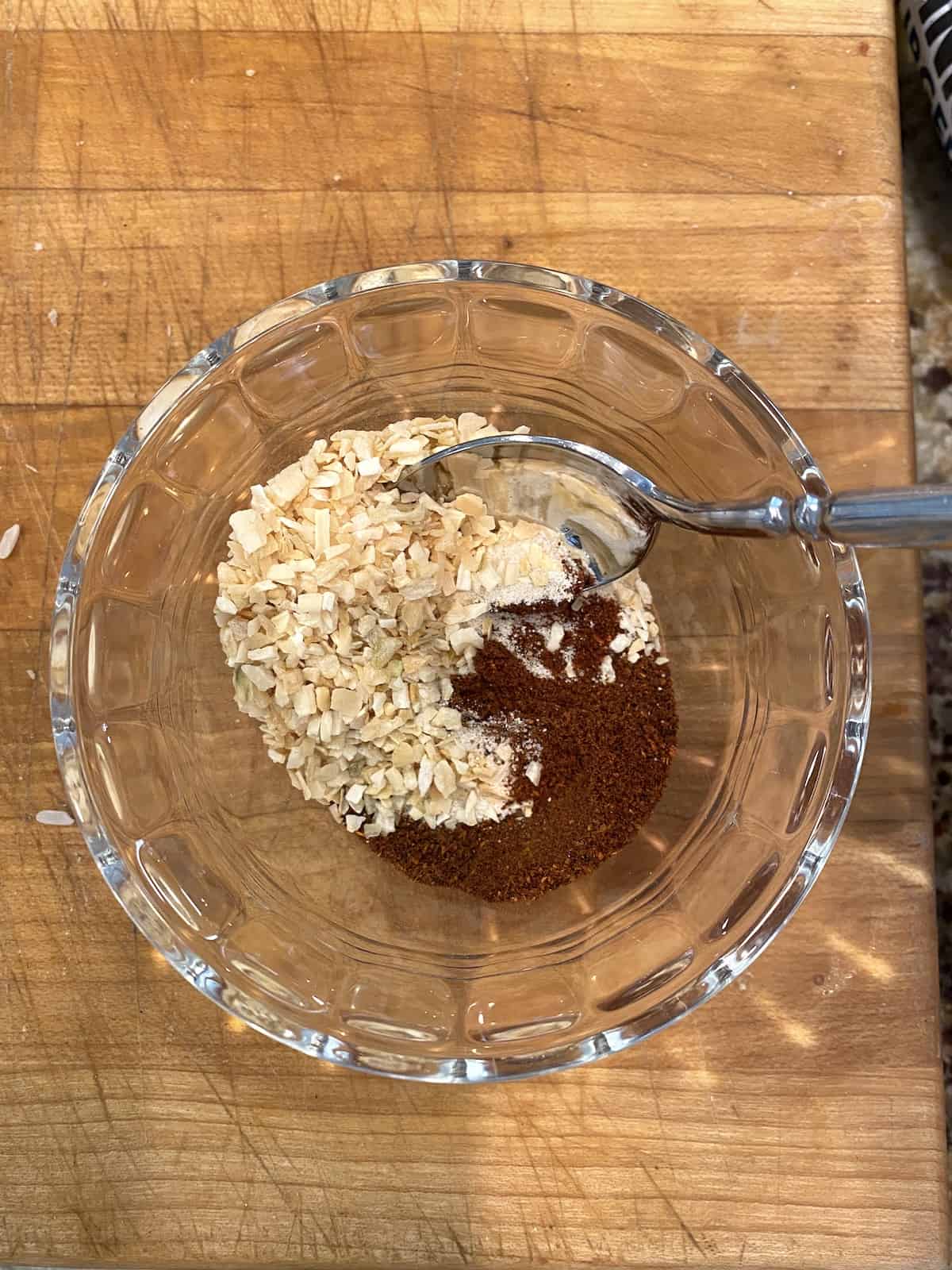 Spices and dried onion in a small bowl with a spoon.