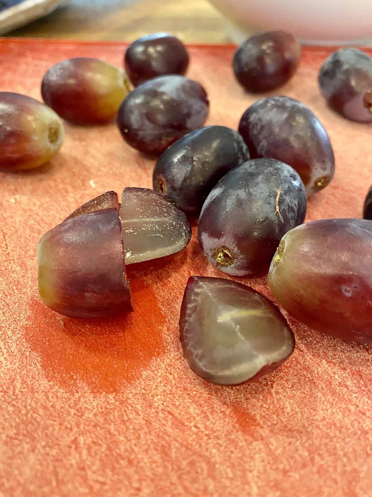 Grapes sliced in half on a cutting board.