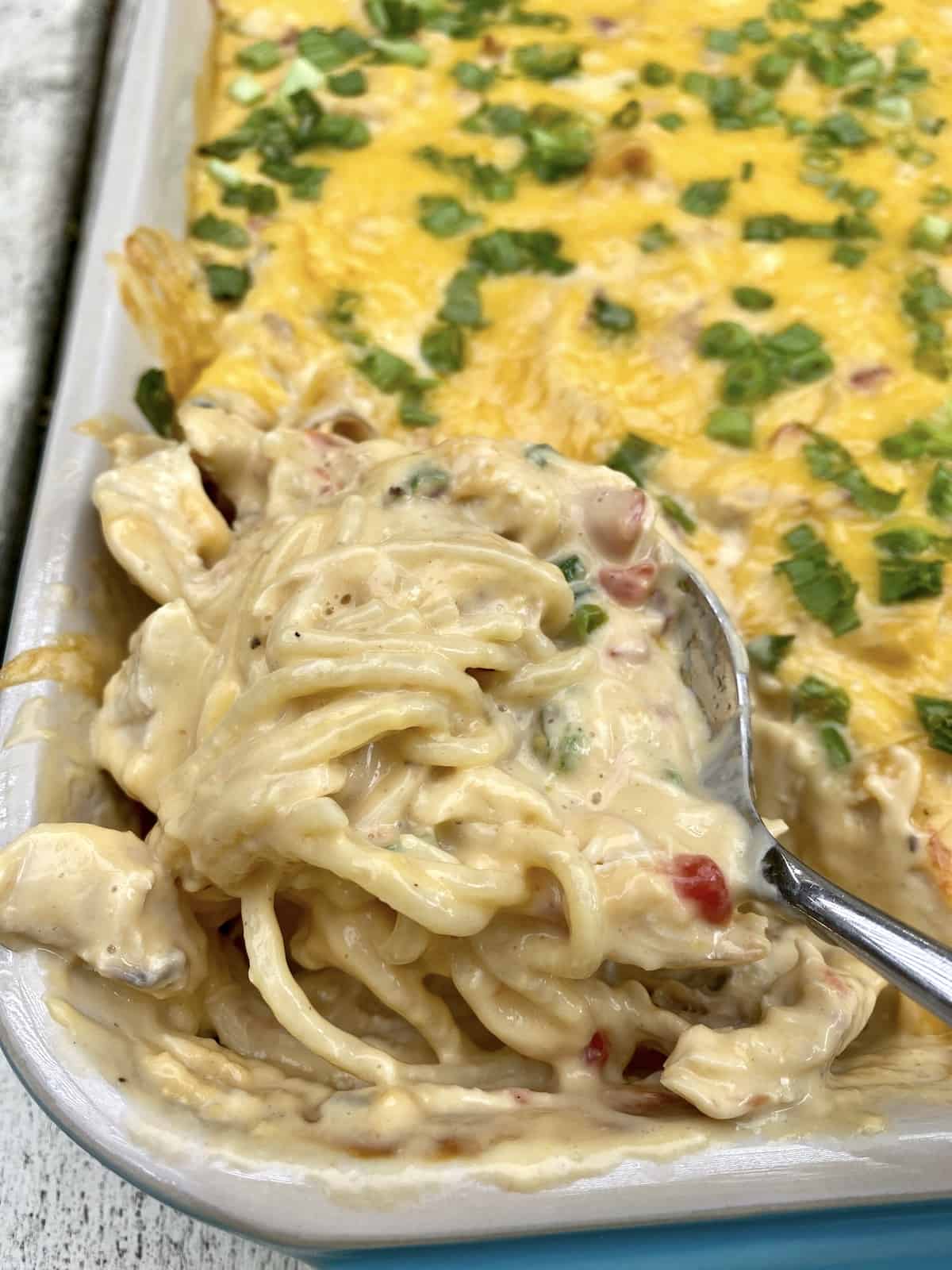 A spoon dishing up chicken spaghetti from a baking dish.