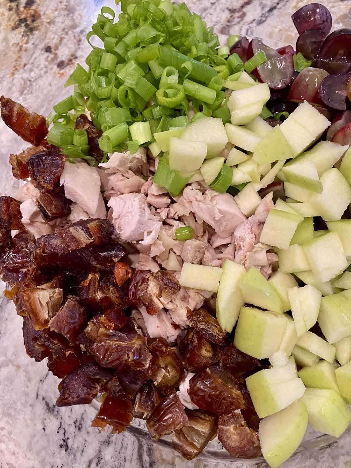 Chicken curry salad ingredients layered next to each other in a bowl.