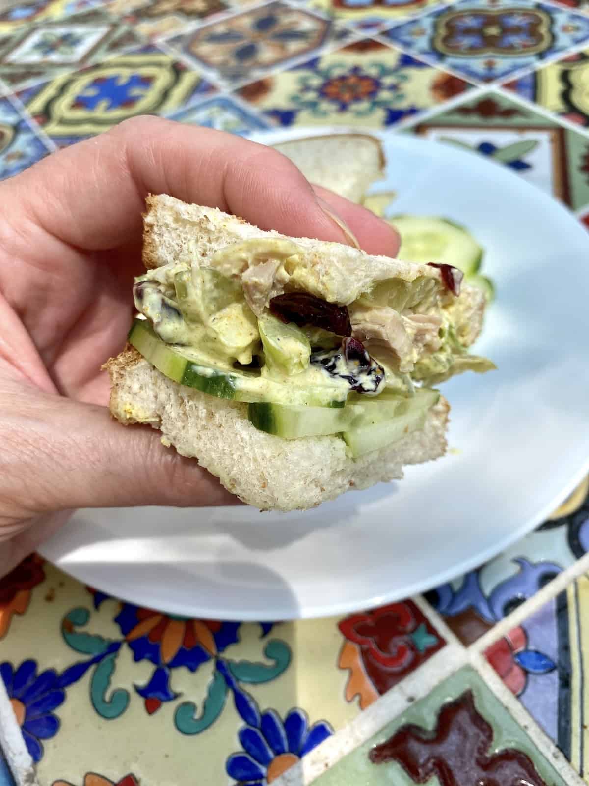 A small chicken curry sandwich, held in a hand over a plate.