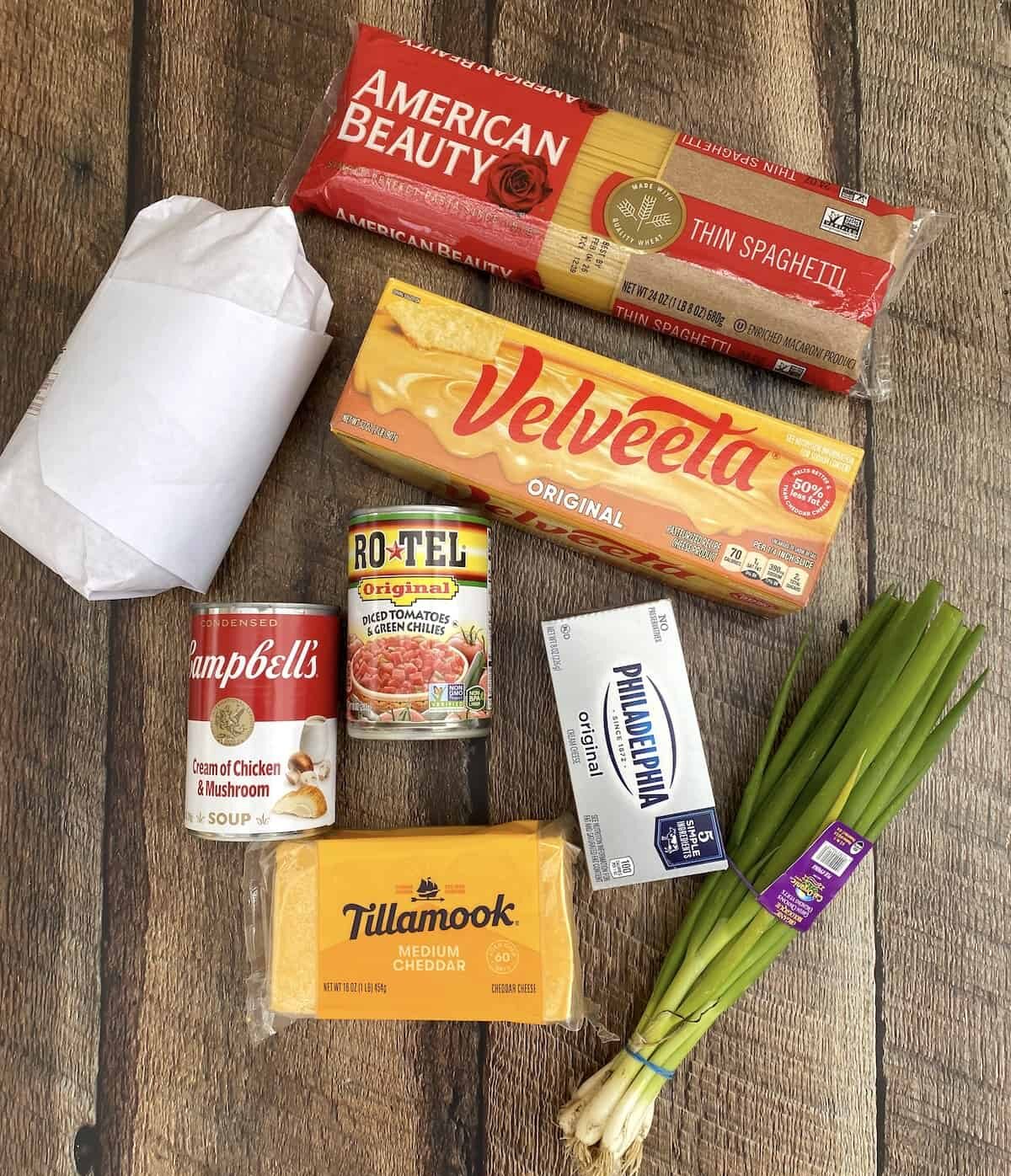 Ingredients for chicken spaghetti with Velveeta and Rotel spread out on a wooden plank.