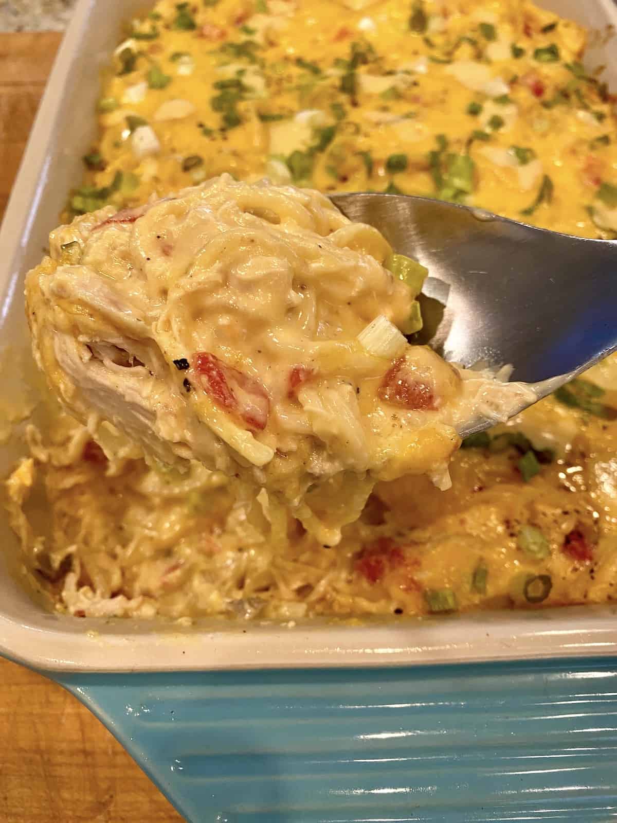 A large spoon, scooping up a serving a chicken spaghetti from a baking dish.