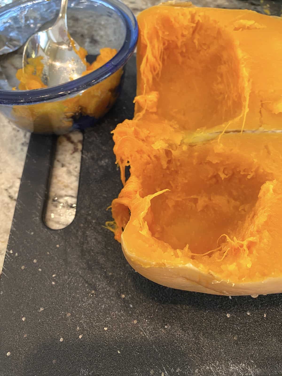 Two halves of butternut squash, cooked, on a cutting board with a small bowl on the side.