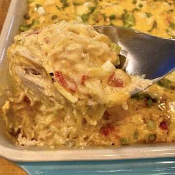 A large spoon, scooping up a serving a chicken spaghetti from a baking dish.