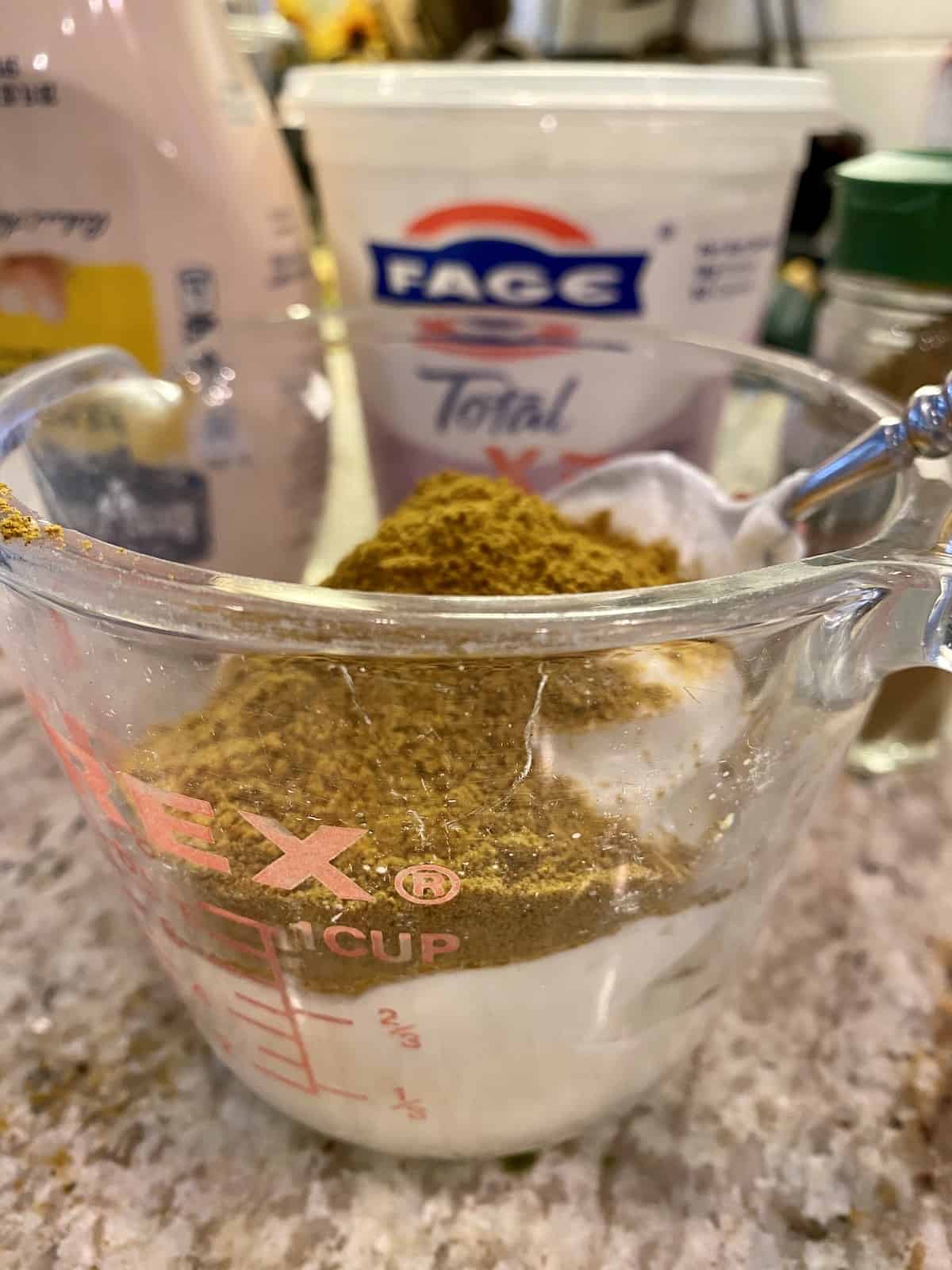 Curry powder on top of Greek yogurt and mayonnaise in a measuring cup.