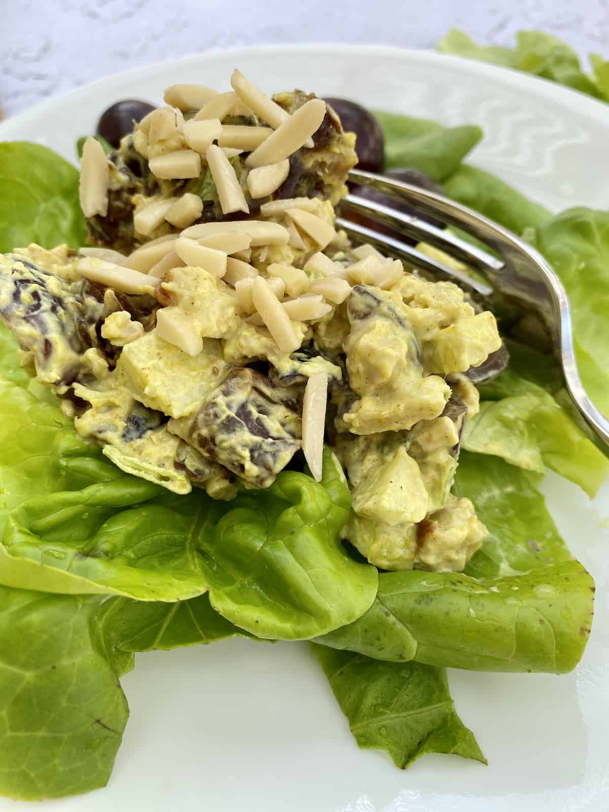 Chicken curry salad on a bed of lettuce on a plate with a fork on the side.