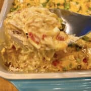 A large spoon dishing up a serving a chicken spaghetti from a baking dish.