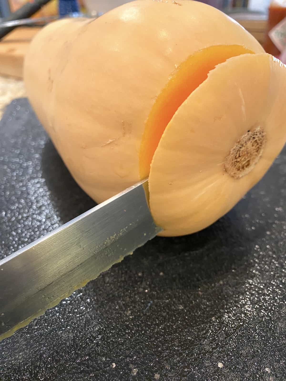 A knife slicing the end off of a butternut squash.