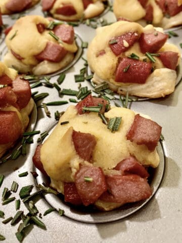 Corn dog nuggets in mini muffin pans with diced rosemary on the edges.