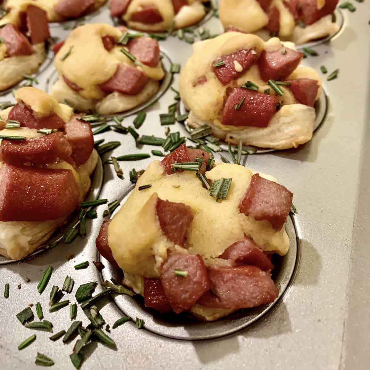 Corn dog nuggets in mini muffin pans with diced rosemary on the edges.