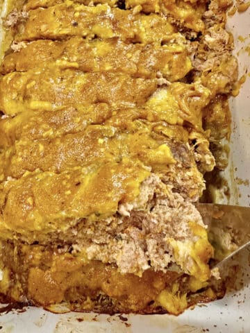A baking dish with a cooked meatloaf, sliced with a spatula lifting out one serving.