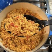 A pot of cooked Mexican fried rice, with a large spoon dishing up a serving of the rice.