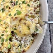 A spoon scooping up twice baked potatoes from a baking dish.