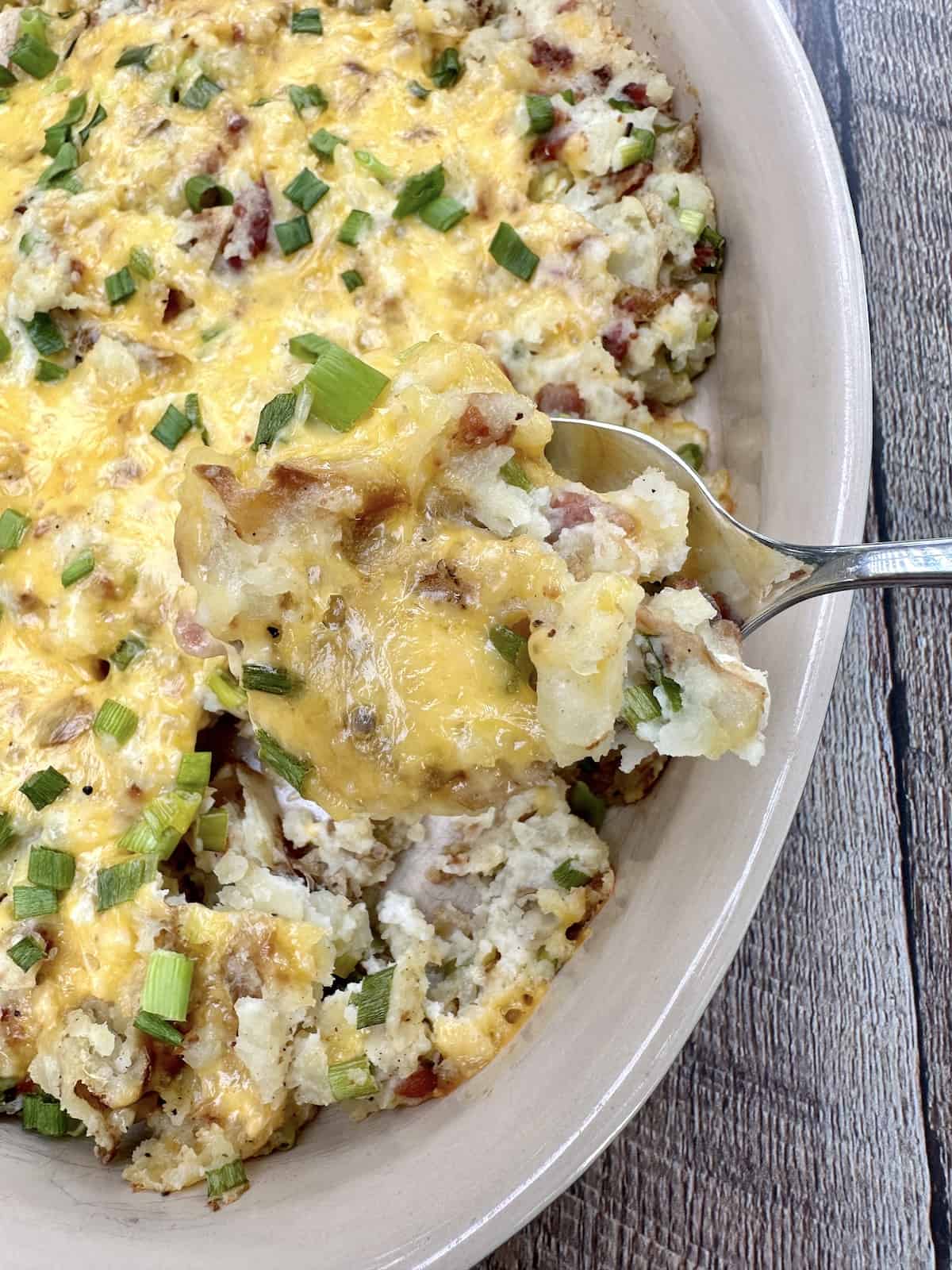 An up close shot of a spoon scooping up twice baked potatoes from a baking dish.