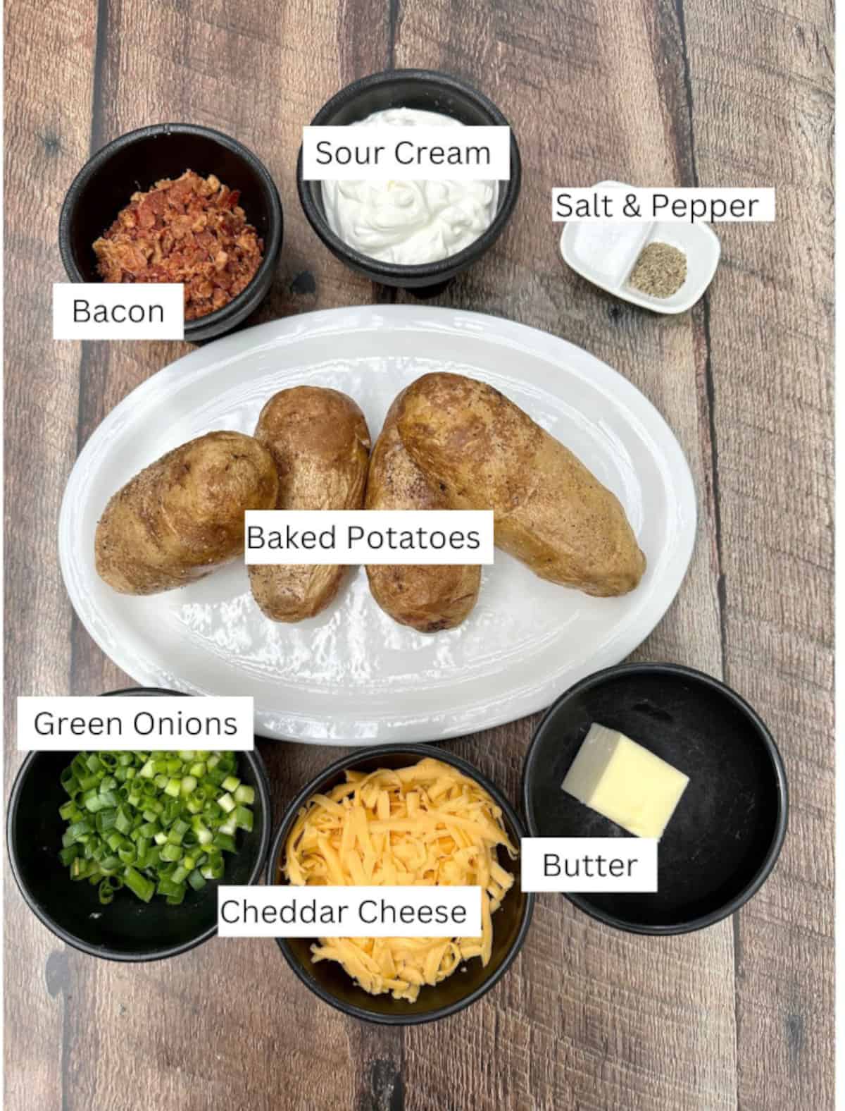 Ingredients for Twice-Baked Mashed Potatoes arranged on a wooden table and labeled.