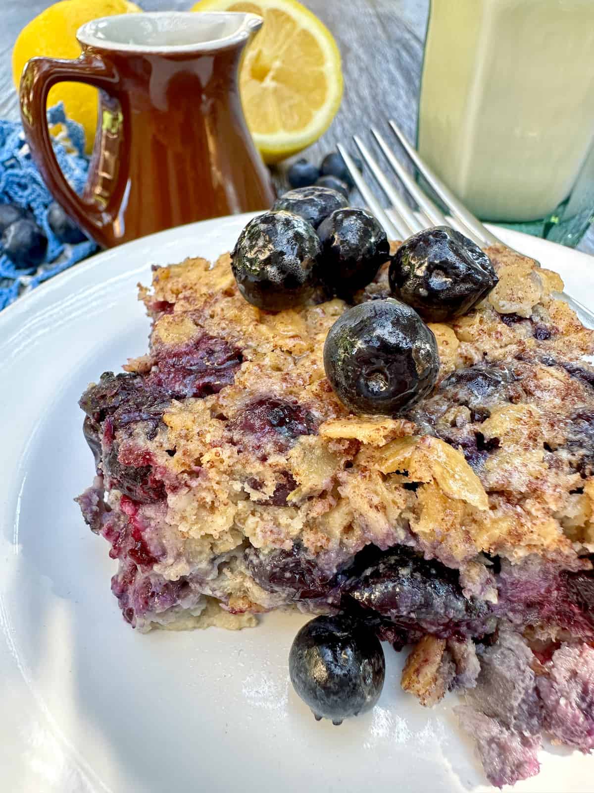 One portion of baked oatmeal with blueberries on the plate and on top with a wedge of lemon in the background.