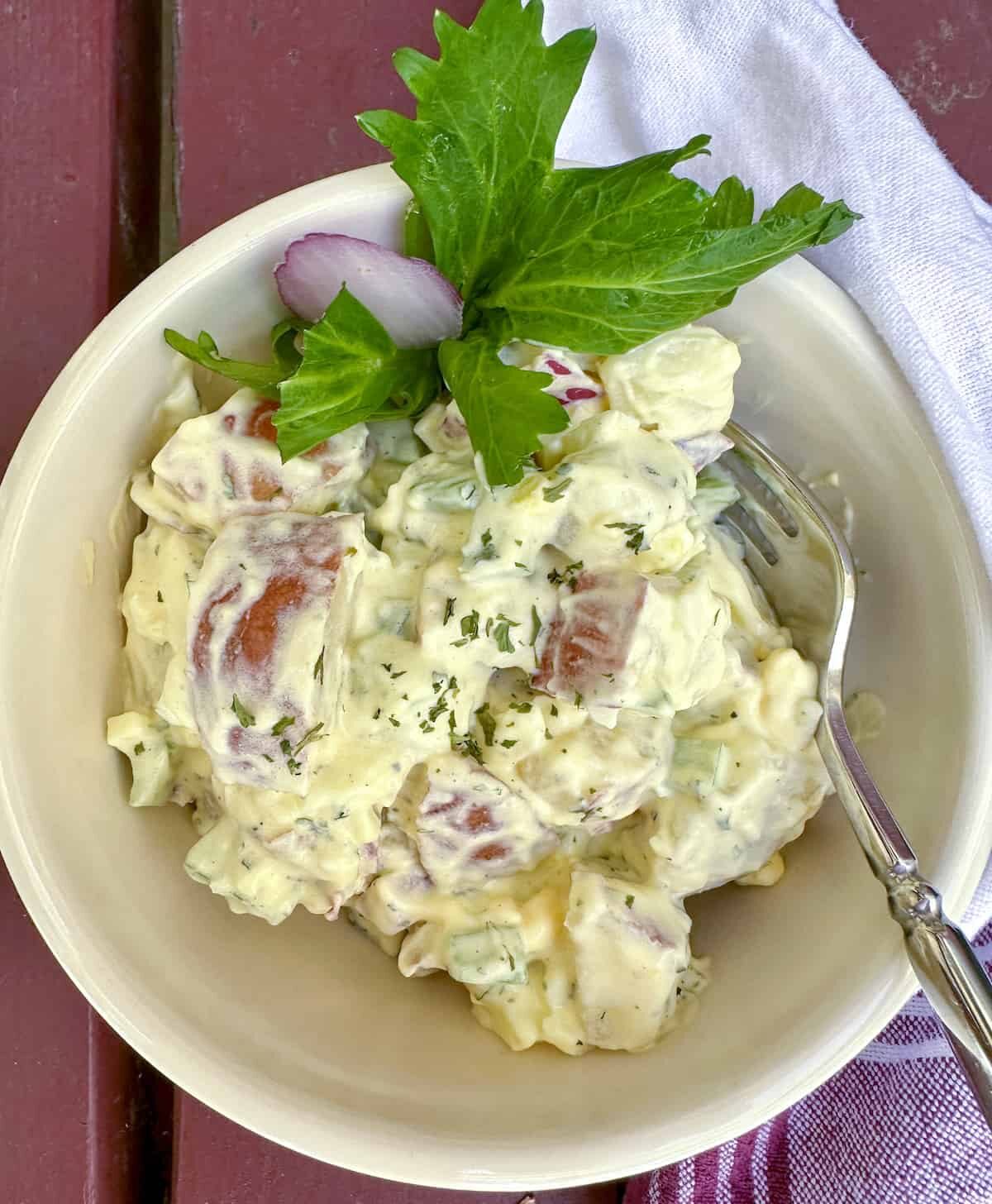 Red potato salad in a small serving bowl with a fork on the side.