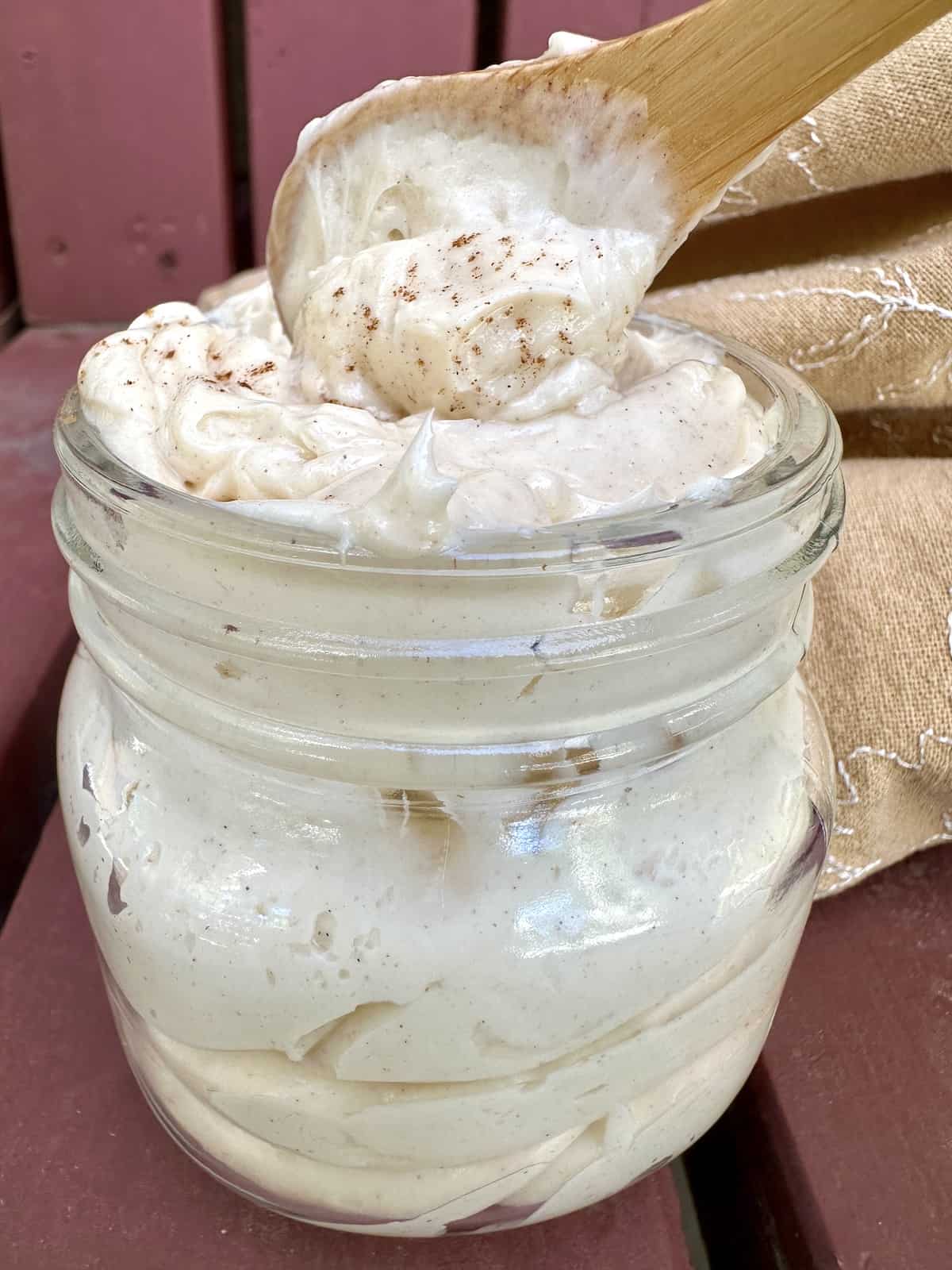 Honey butter in a jar with a napkin on the side and a spoon dishing up a small portion of butter.