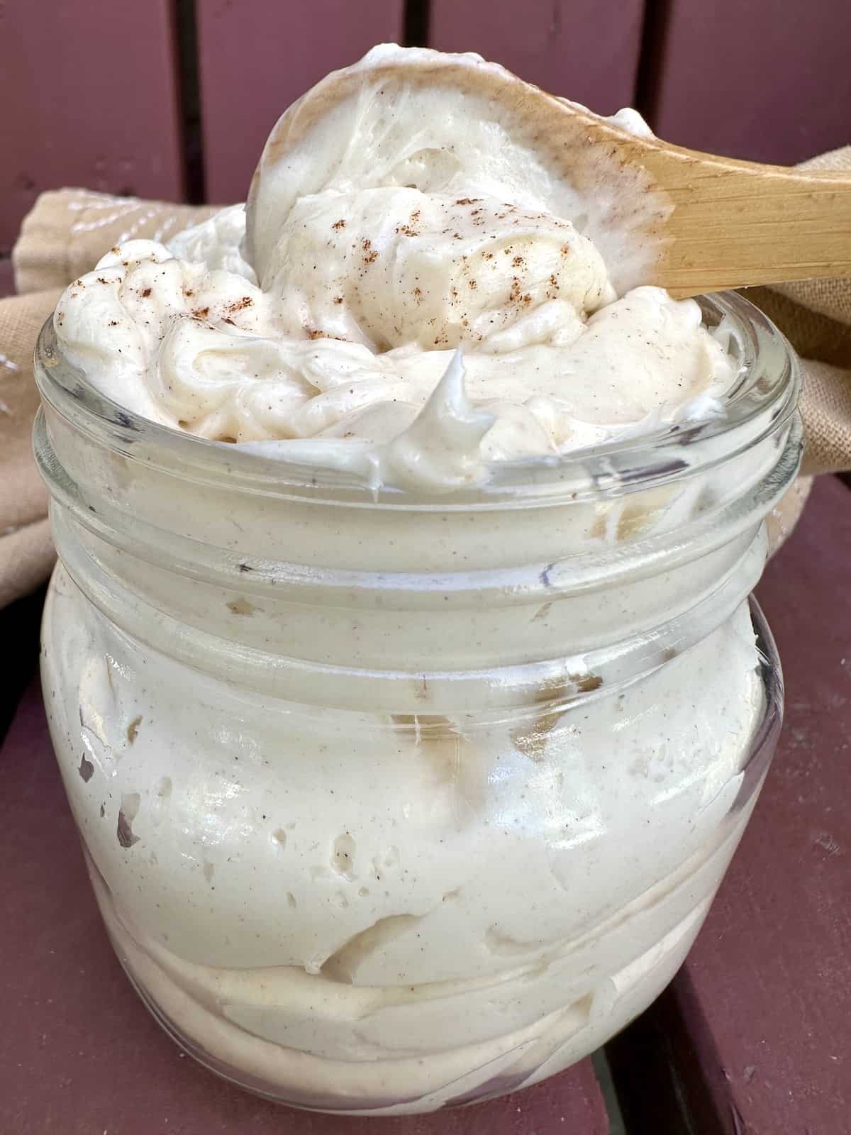 A small jar full of whipped honey butter with a spoon on top scooping up a portion of butter.