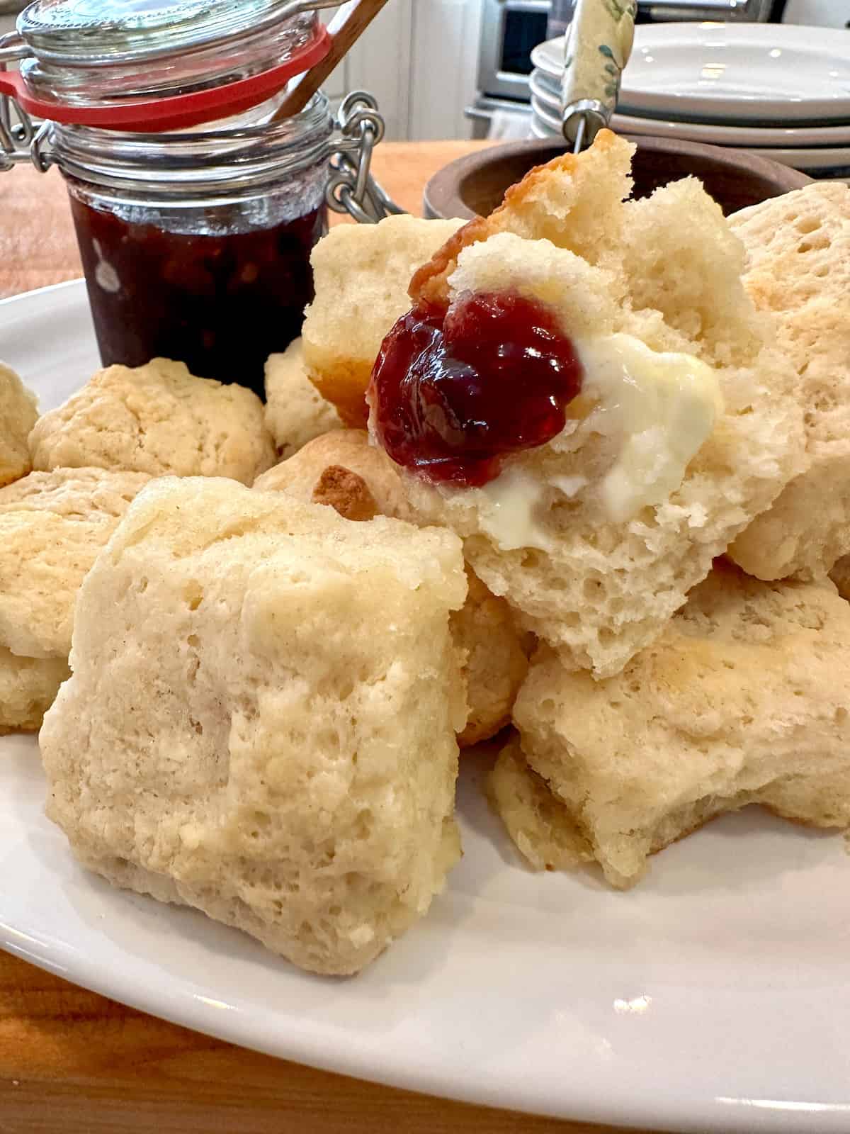Biscuits on a plate with a portion of jam on one biscuit and a jar of jam.