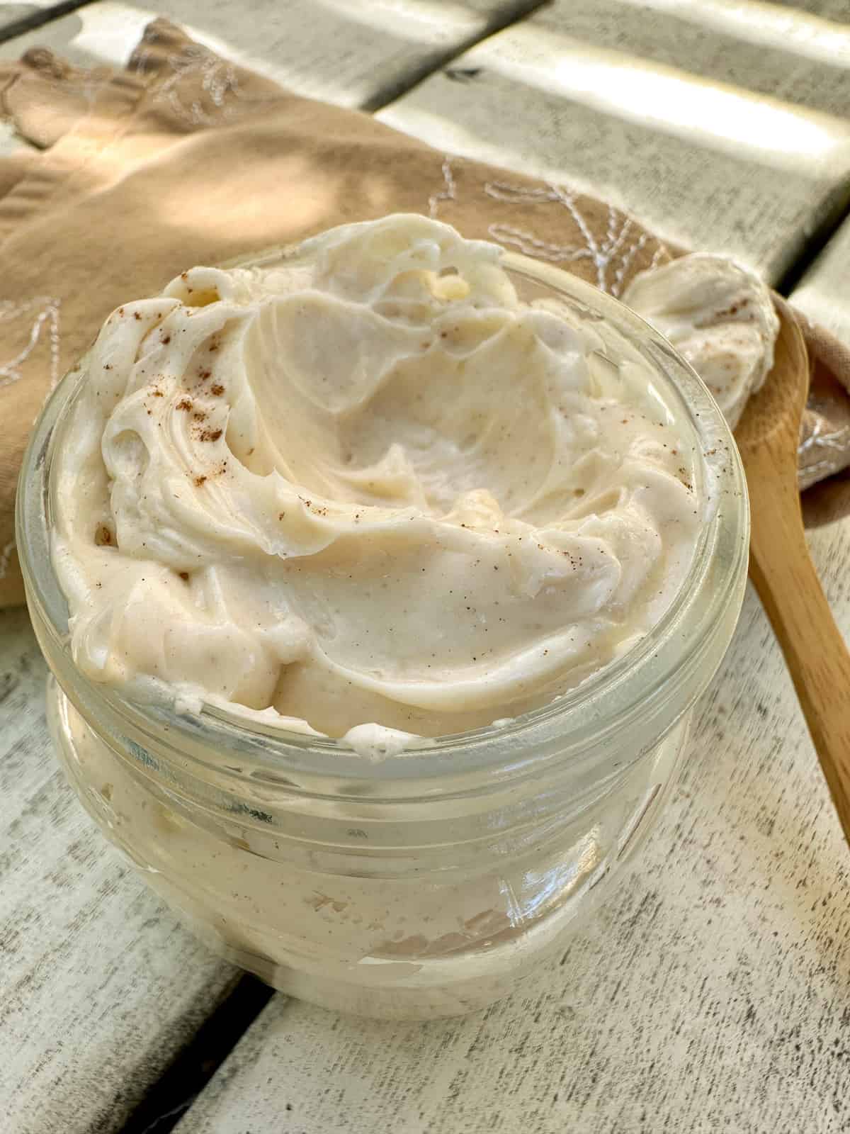 Honey butter in a small jar on a table with a wooden spoon on the side of the jar.