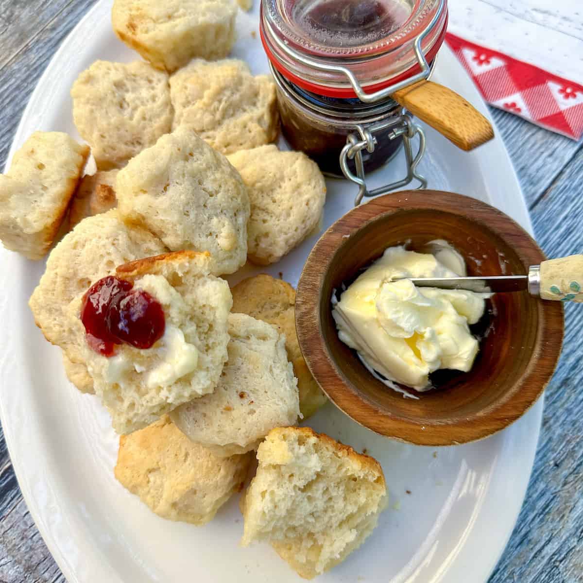 Baked biscuits on a plate with a bowl of butter and jar of jam.