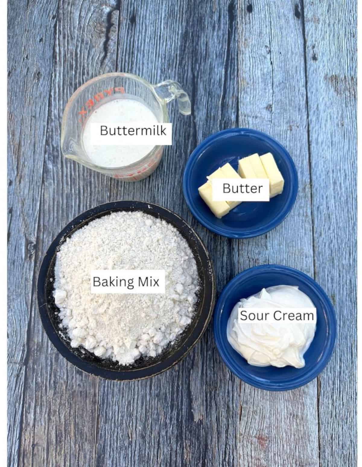 Ingredients for basic biscuits in containers arranged on a wooden plank.