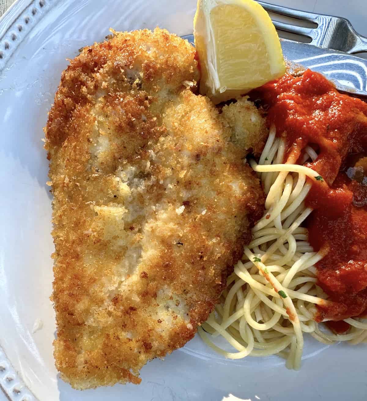 Cooked Chicken Romano on a plate with spaghetti on the side topped with sauce.