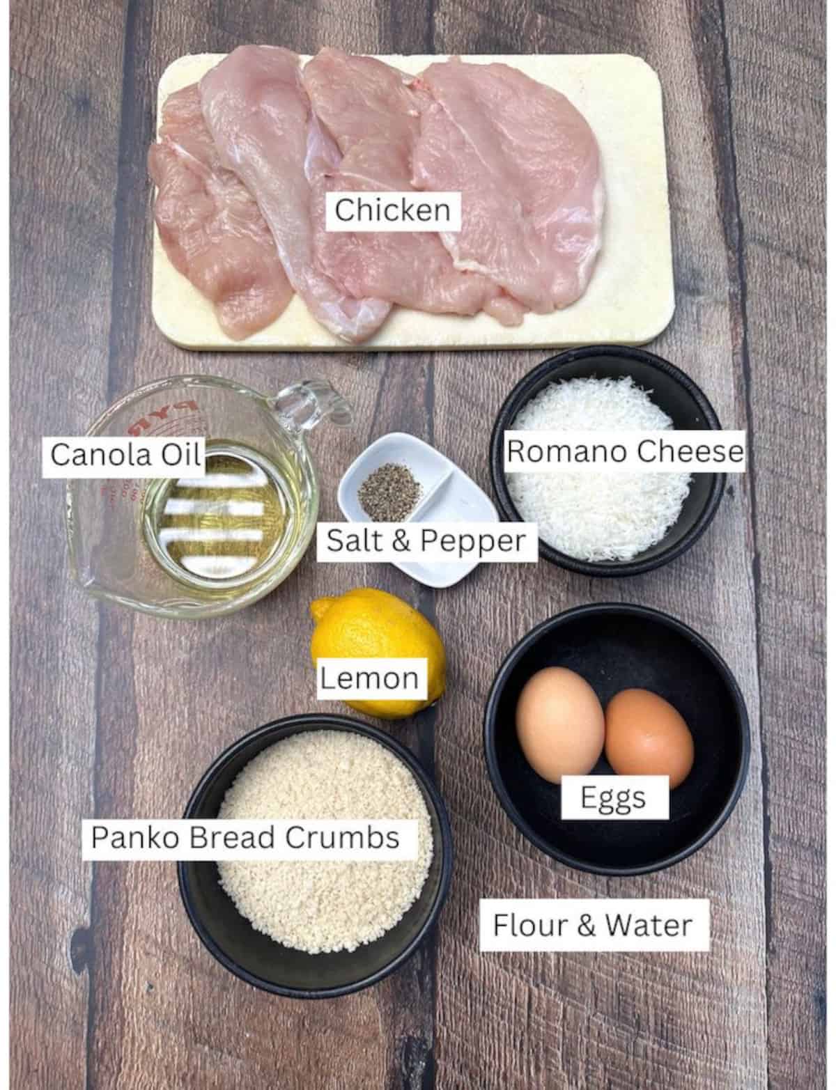 Ingredients for chicken Romano in small dishes and bowls on a wooden plank.