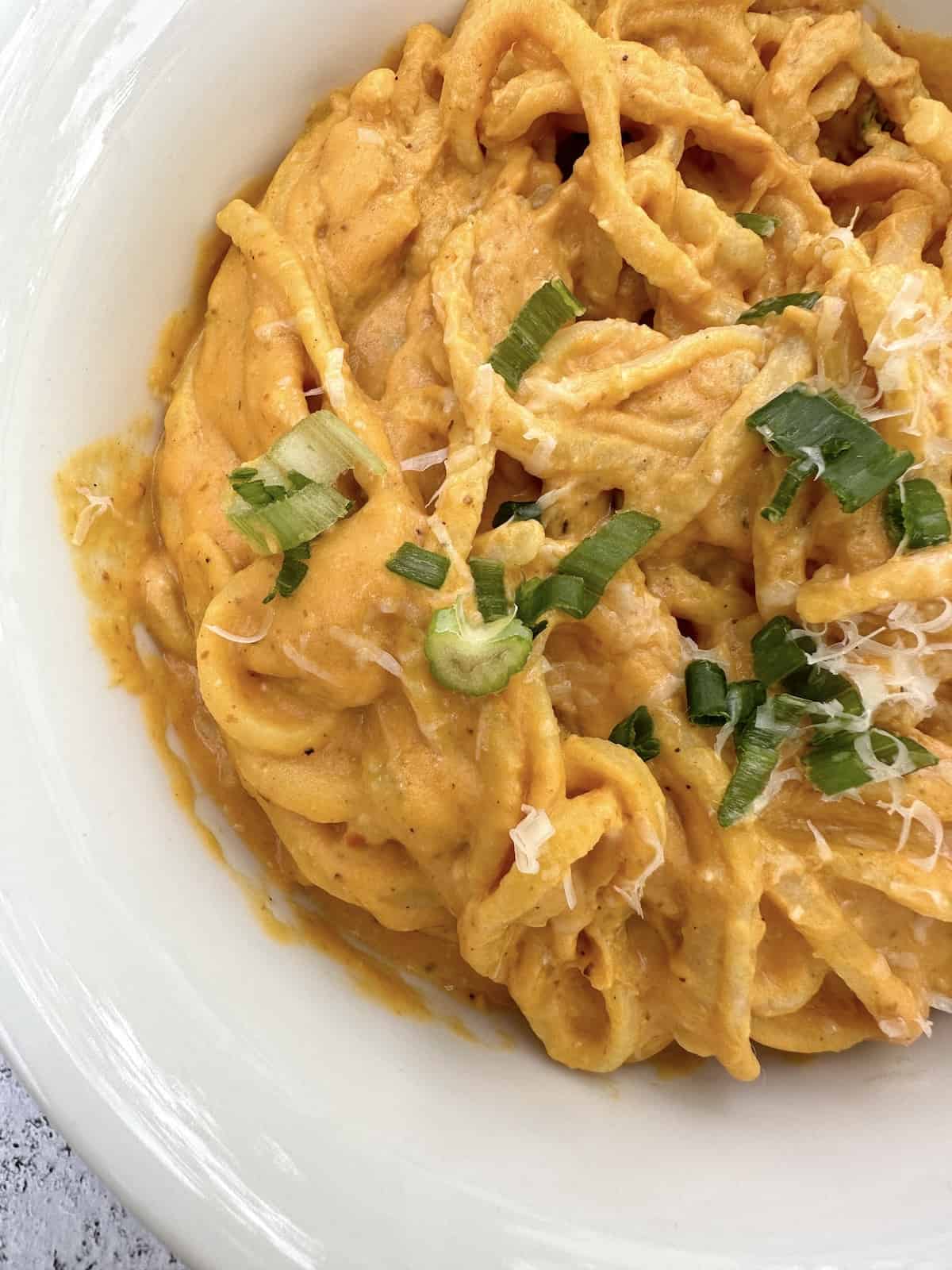 Pumpkin sauce and pasta in a bowl topped with diced onions and cheese.