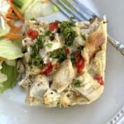Chicken casserole on a plate with salad on the side and a fork on the plate.