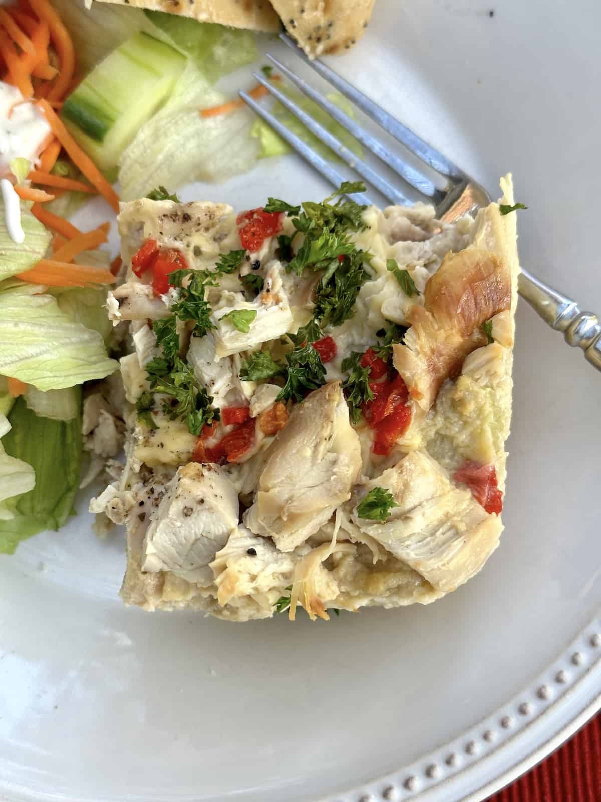 Chicken casserole on a plate with salad on the side and a fork on the plate.