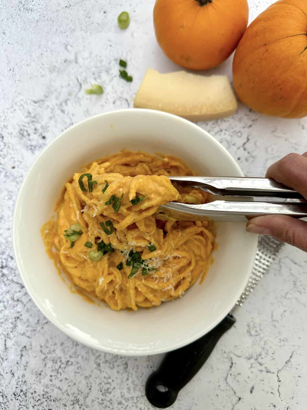 Pumpkin sauce with pasta in a bowl with pumkins and a wedge of parmesan cheese on the side.