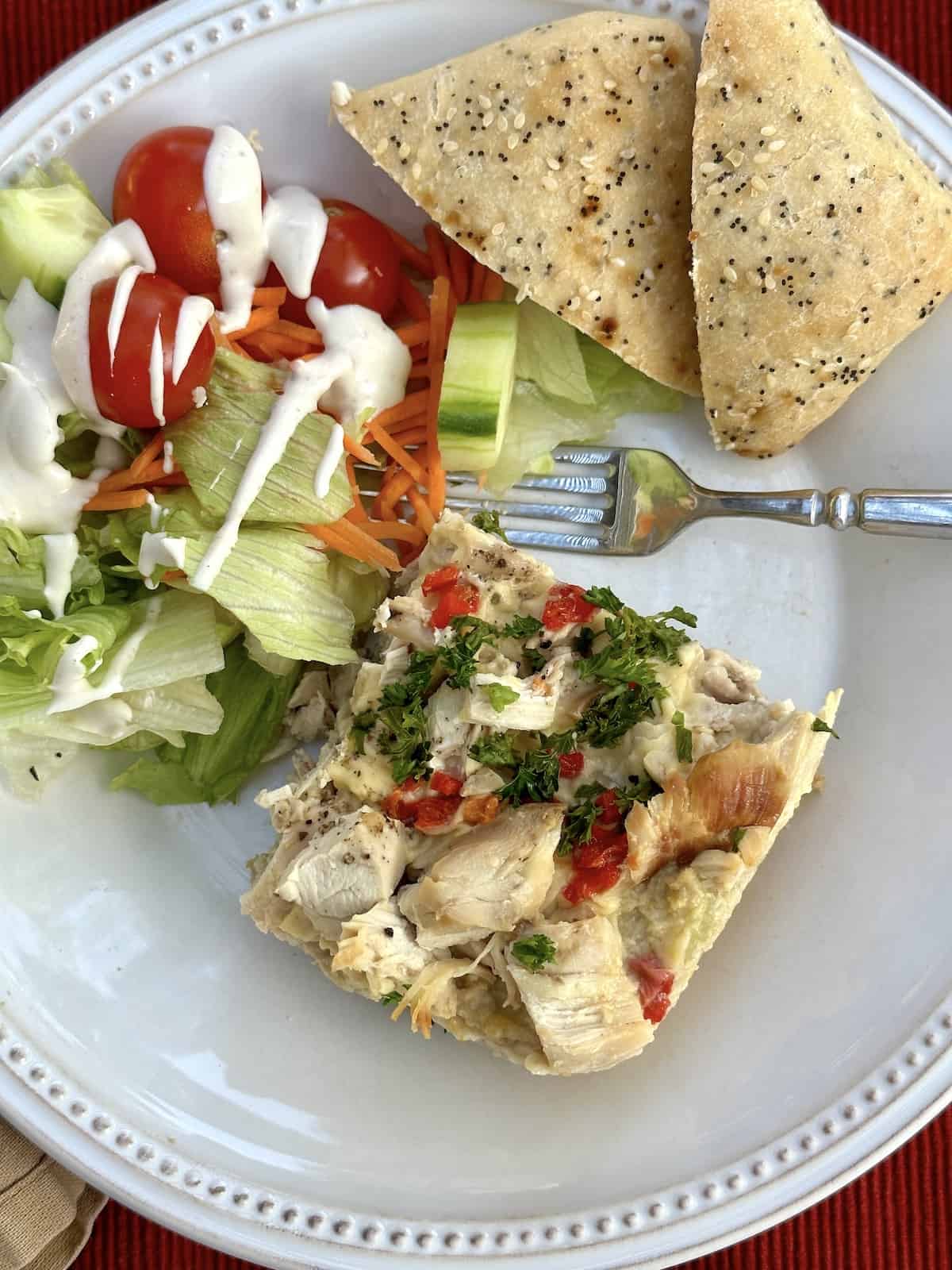 Chicken casserole on a plate with rolls and a side salad.