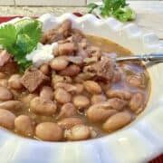 A serving of pinto bean chili in a bowl with a spoon and garnishes on the side.